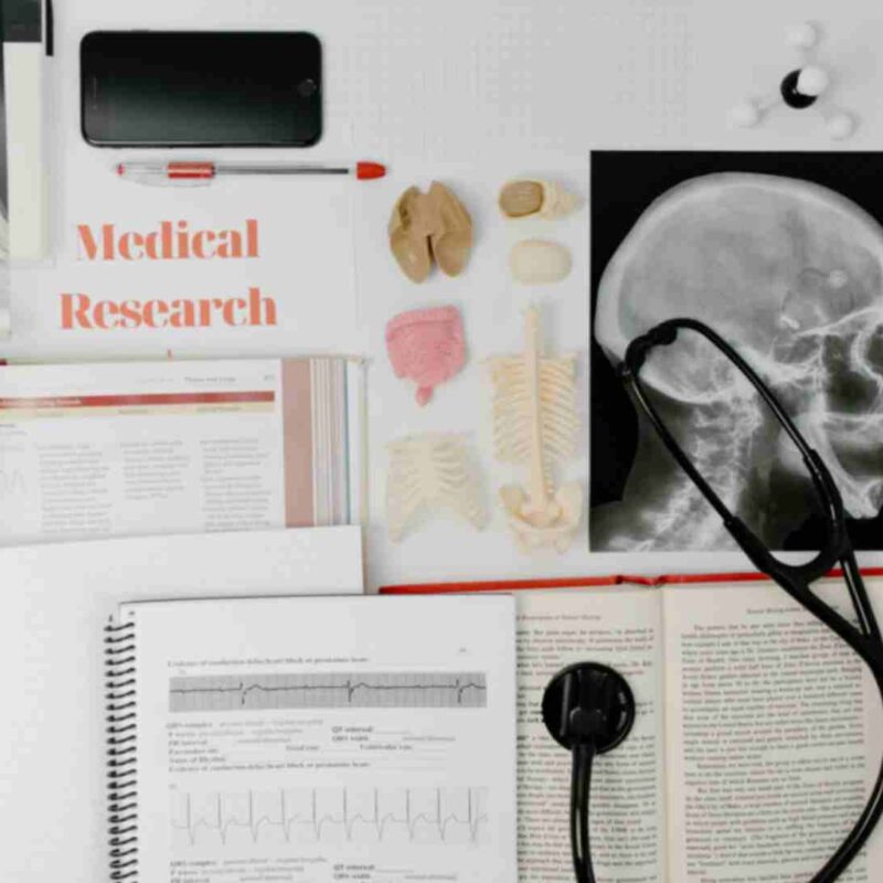 Medical research materials, including anatomy models, an X-ray image of a skull, medical textbooks, a stethoscope, and a phone, representing the study and practice of healthcare.