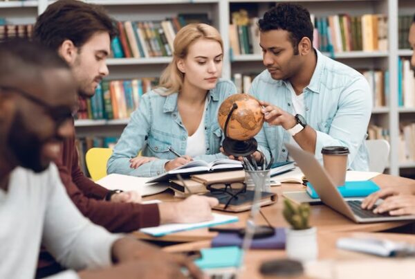 Group of diverse researchers collaborating in a library, studying with books, a globe, and laptops, symbolizing global academia.