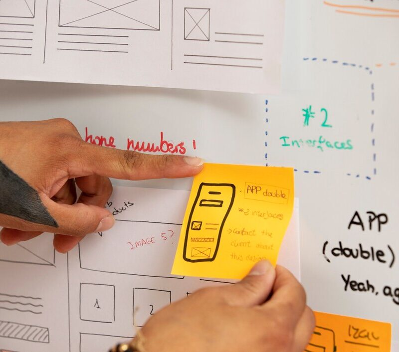 Close-up of hands holding a post-it note with a mobile app prototype design, symbolizing innovation and planning for technology development.