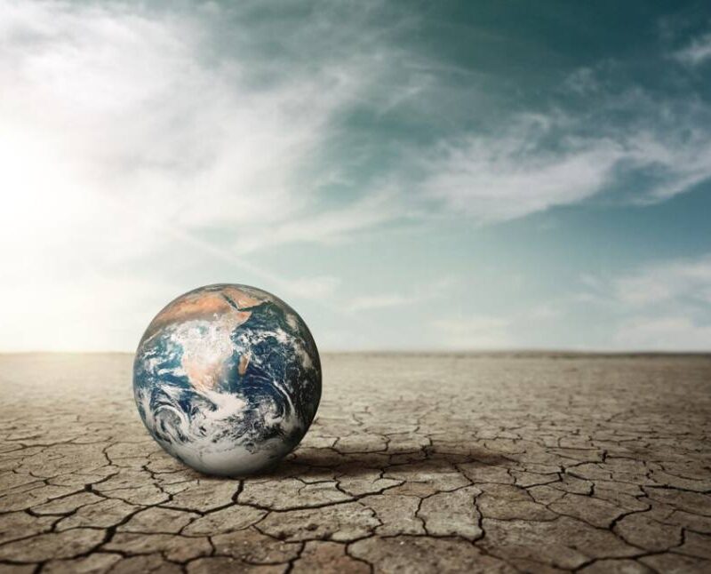 Earth on cracked dry ground under a vast sky, symbolizing the impact of climate change and the need for resilience initiatives.