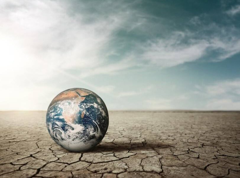 Earth on cracked dry ground under a vast sky, symbolizing the impact of climate change and the need for resilience initiatives.