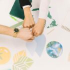 Three hands fist-bumping over a desk with environmental symbols, representing teamwork in global climate action projects.