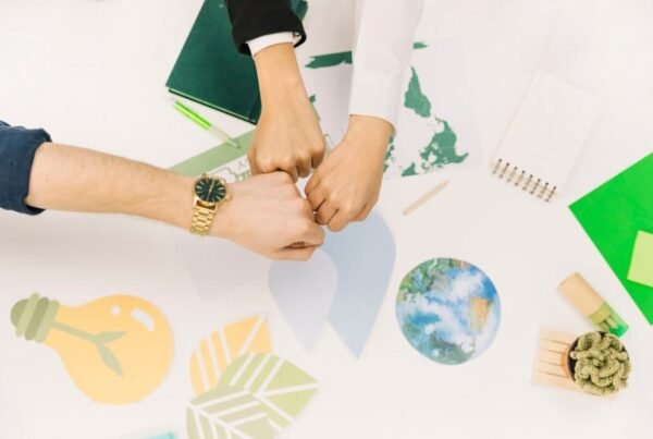 Three hands fist-bumping over a desk with environmental symbols, representing teamwork in global climate action projects.