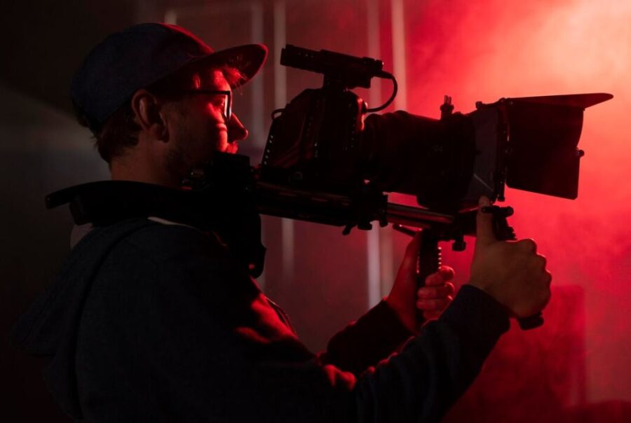 Filmmaker using a professional camera in a red-lit setting, capturing impactful visuals for a documentary film.