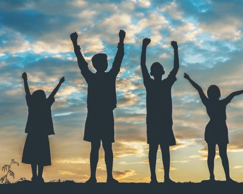 Silhouette of four people raising their arms in triumph against a scenic sky, symbolizing empowerment, collaboration, and growth.