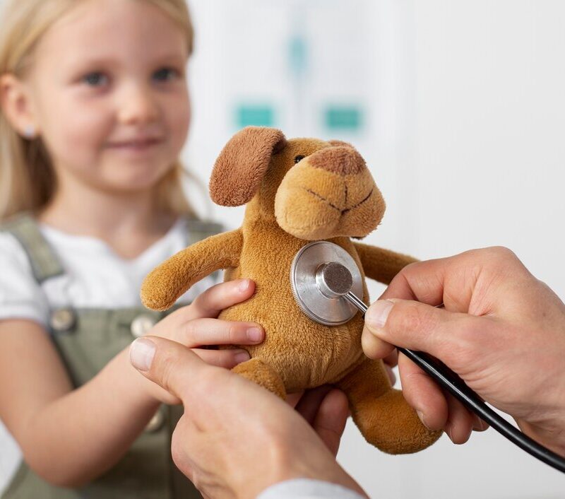 A young girl holds a stuffed toy while a pediatrician uses a stethoscope, symbolizing child healthcare and support for pediatric programs.
