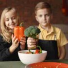 Two children holding fresh vegetables, symbolizing the importance of nutrition and early childhood health development.