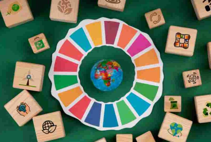 A colorful representation of the UN Sustainable Development Goals surrounding a globe, with wooden blocks featuring sustainability icons, symbolizing global social impact initiatives.